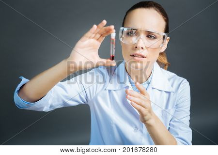Allery testing. Top view on a female medical professional in special glasses lifting a test tube with a blood sample and looking at it attentively.