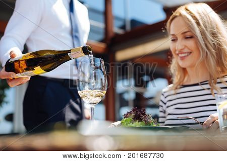 Excellent choice. Selective focus of white semisweet wine being poured into a glass by a nice skillful handsome waiter