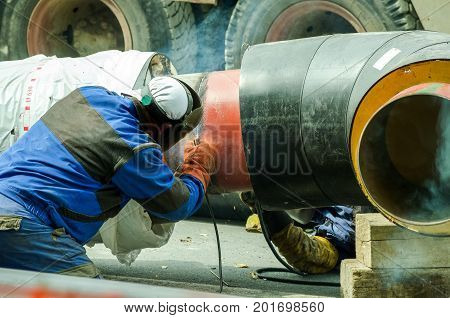 Welder welds pipe for district city heating system on the street with selective focus.