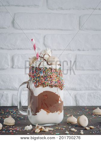 Close up view of freakshake in mason jar on brown table. Freaked milkshake with chocolate, biscuit cookies and sugar sprinkling. Copy space. Trendy food concept. Vertical.