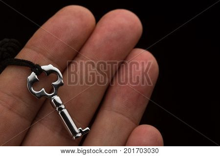 top view closeup of Caucasian hand holding a small silver lock key with dark fabric thread on black background