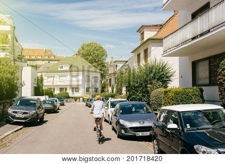 STRASBOURG FRANCE - JUL 29 2017: French elegant woman cycling in calm neighborhood with cars parked and beautiful French real estate architecture houses