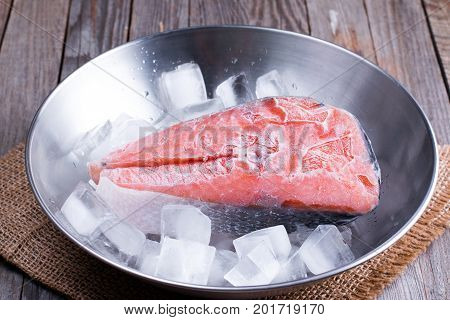 frozen red fish steaks with ice on a wooden background