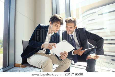 Mature businessman using a digital tablet to discuss information with a younger colleague in a modern business office