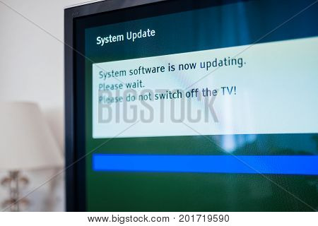 System update software process on a modern television set in living room with message System software is now updating please wait. Please do not switch off your tv. Tilt-shift lens used