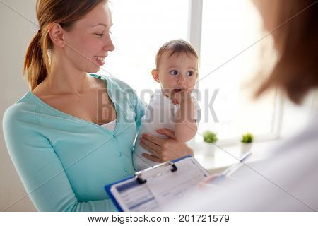 medicine, healthcare, pediatry and people concept - happy woman with baby and doctor with clipboard at clinic