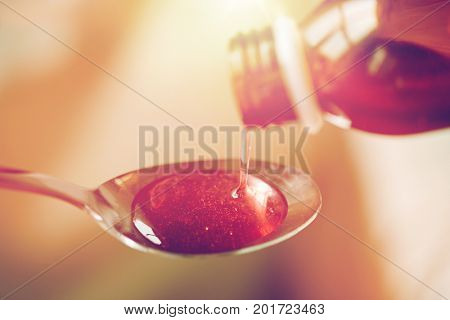 healthcare, treatment and medicine concept - bottle of medication or antipyretic syrup and spoon