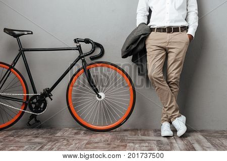Cropped image of dressed half mens body standing near a bicycle isolated over gray background