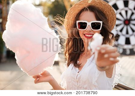 Close up portrait of a pretty young girl in sunglasses eating cotton candy at amusement park