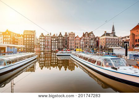 Morning view on the beautiful buildings and boats on the Damrak avenue in Amsterdam