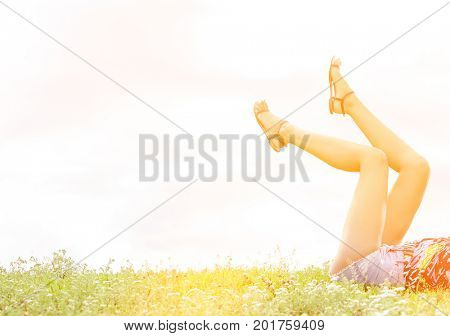 Low section of woman with feet up lying on grass against sky