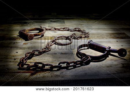 Old fashioned, vintage shackles on a rustic wooden background. The picture is reflective of incarceration, jail, kink, bound, rust, corrosion, cuffs, vintage, law enforcement, antiques