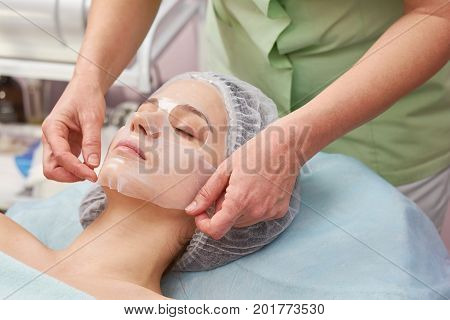Female face, hands of cosmetician. Woman with hydrogel mask.