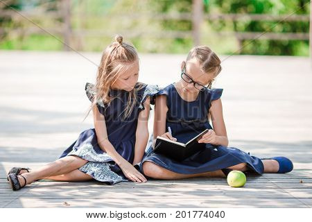 Adorable little school girls with notes and pencils outdoor.
