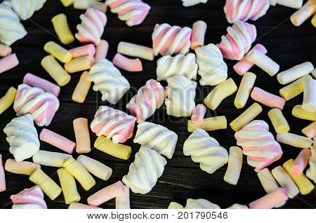 Multicolored Marshmallow Background on Black Wooden table. Background of multi-colored and different in shape and size of marshmallows. Sweets background