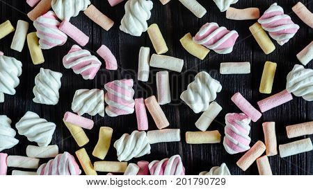 Multicolored Marshmallow Background on Black Wooden table. Background of multi-colored and different in shape and size of marshmallows. Sweets background