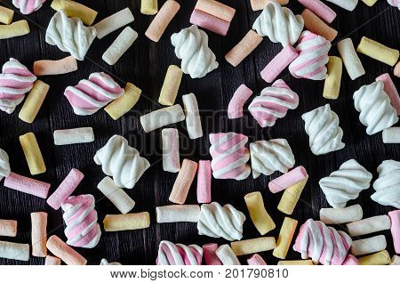 Multicolored Marshmallow Background on Black Wooden table. Background of multi-colored and different in shape and size of marshmallows. Sweets background