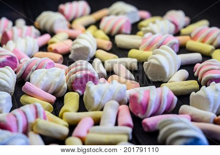 Multicolored Marshmallow Background on Black Wooden table. Background of multi-colored and different in shape and size of marshmallows. Sweets background