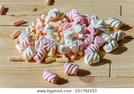 Multicolored marshmallows on bright wooden table. Background of multi-colored and different in shape and size of marshmallows. Sweets background