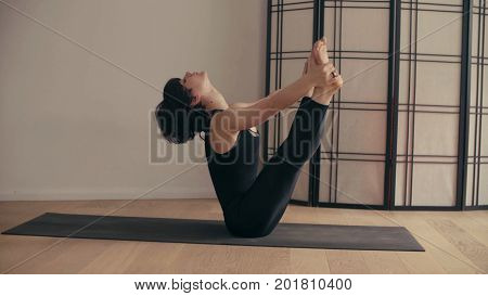 A young woman performing yoga-asanas in the hall. Paripurna Navasana. Halassana