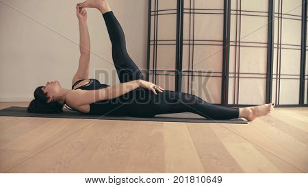 A young woman performing yoga-asanas in the hall. Supata padangushthasana