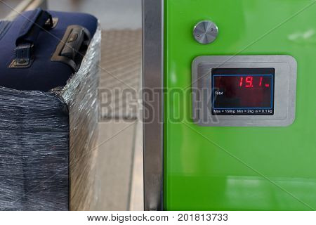 Checking the weight of luggage in the airport during the check-in by low cost airlines restrictions. Wrapping baggage before travel by airplane. Suitcase in protective transparent film.