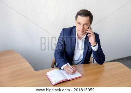 serious business man in office making cell phone call and taking notes.