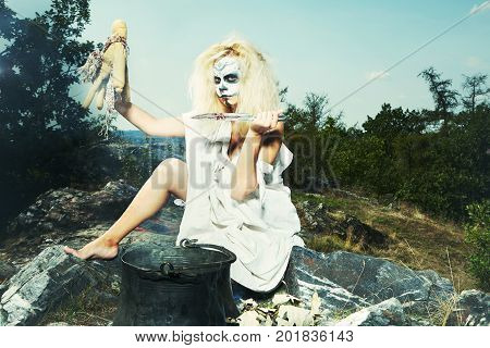 Young blonde witch during black magic voodoo ritual spelling some person through fetish doll
