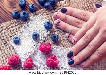 bog whortleberry raspberries and female hands with black and pink art manicure on a sackcloth and wooden background