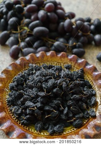 A bunch of fresh sweet dark and succulent raisins poured into a dish grapes lying in a table.