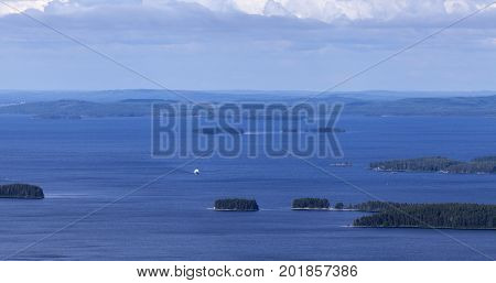 View of a vast lake, islands and islets. White ship approaching, woodland up North.