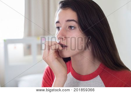 Teenage Girl Sitting In Bedroom Biting Nails