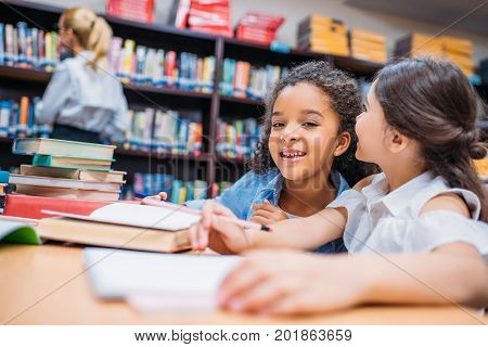 two happy little schoolgirls gossiping at library