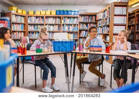 beautiful little kids sitting at desk in library