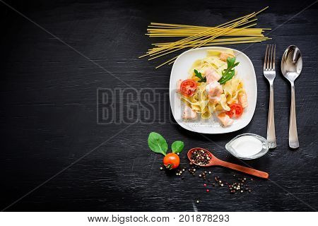Food concept with tasty pasta with salmon and tomato on dark background. Flat lay, top view.