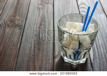 A glass of sugar crystals or cubes on a dark brown wooden table. Intake of bad calories.