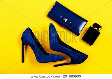 Purse and shoes in dark blue color with black perfume. Accessories in formal style for women isolated on yellow background top view. Clutch and footwear with bottle of scent. Classic fashion concept