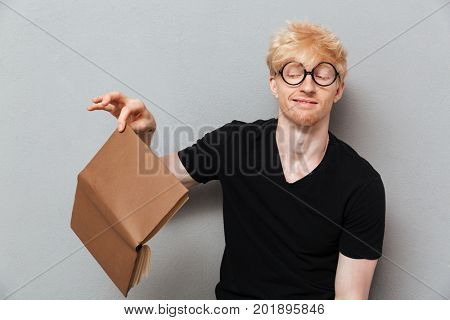 Picture of disapointed caucasian man over grey wall near copyspace. Looking aside holding book.