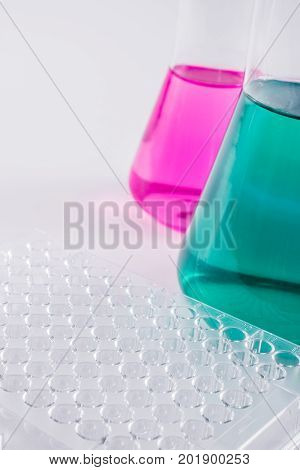 research, science and clinic background. 96 well micro plate and  laboratory beakers with colorful liquids and reagents.