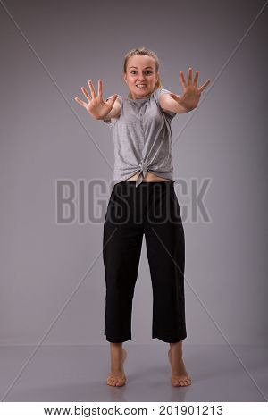 Prohibition symbol. Smyling female shows stop sign talk to hand gesture. Full height portrait of young girl over gray background