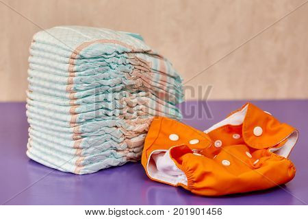 Stack of disposable diapers or nappies on purple background and reusable one