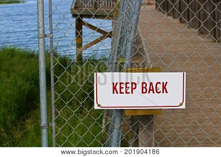 A keep back sign on a chain-link fence.