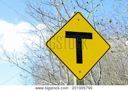 A warning T crossing road sign against trees