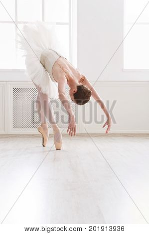 Beautiful graceful ballerina practice in tutu skirt near large window in white light hall. Classical ballet dancer at dance class, side view, copy spce