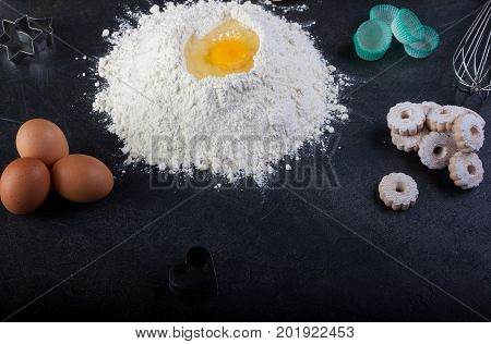 Flour eggs and canestrelli Italian shortbread cookies cooking utensils on black table