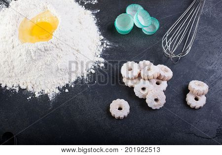 Flour eggs and canestrelli Italian shortbread cookies cooking utensils on black table
