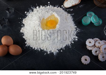 Flour eggs and canestrelli Italian shortbread cookies cooking utensils on black table