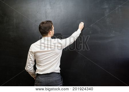 Man in suit pointing something on chalkboard,back view,isolated.Copyspace blank.Teacher writing on black board