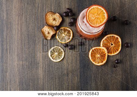 Cocktail on rustic wood background. Cold citrus alcohol beverage with tequila, blood orange juice and ginger beer, served with ice, citrons and chocolate snacks, top view, copy space