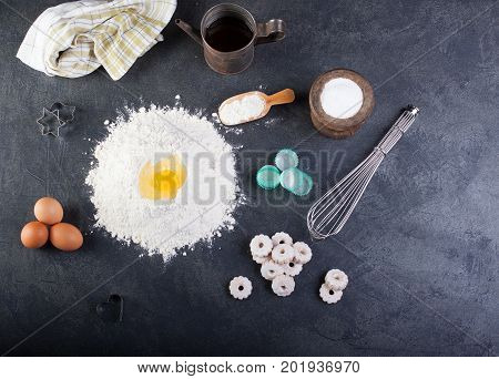 Flour eggs and canestrelli Italian shortbread cookies cooking utensils on black table